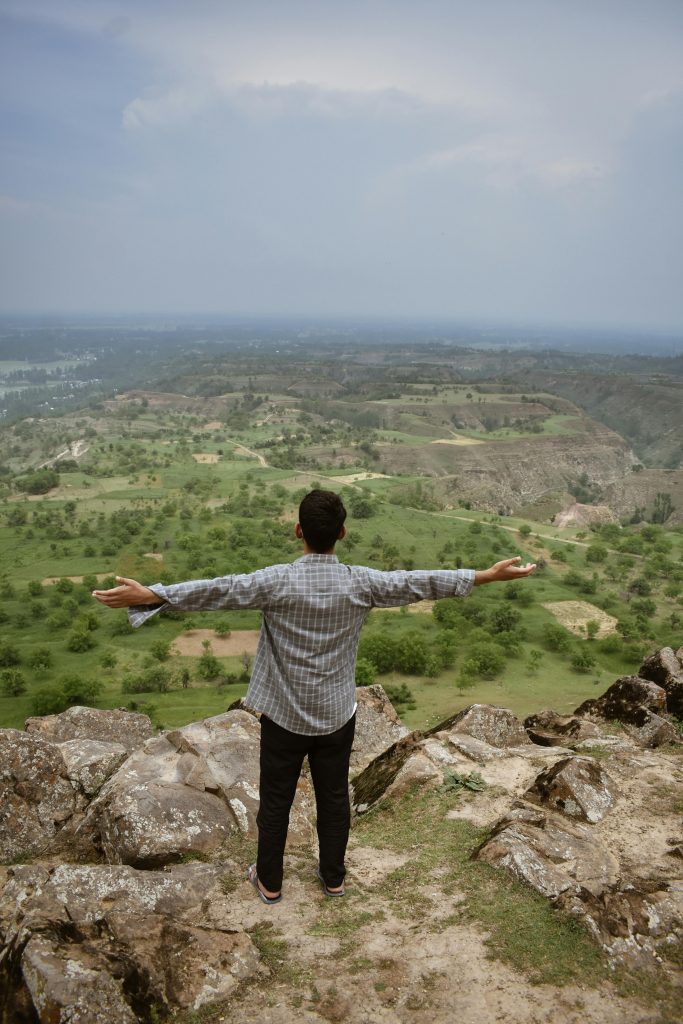 A man stands on a clifftop with arms outstretched, embracing the vast landscape.